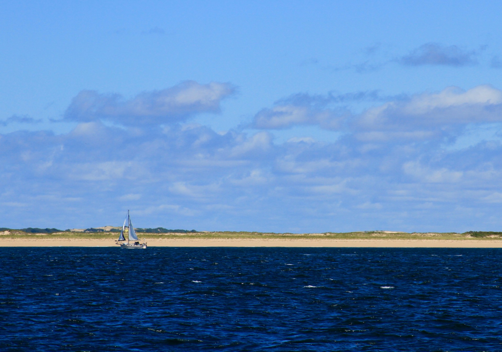Sailboat on blue water with sandy shore, Cape Cod